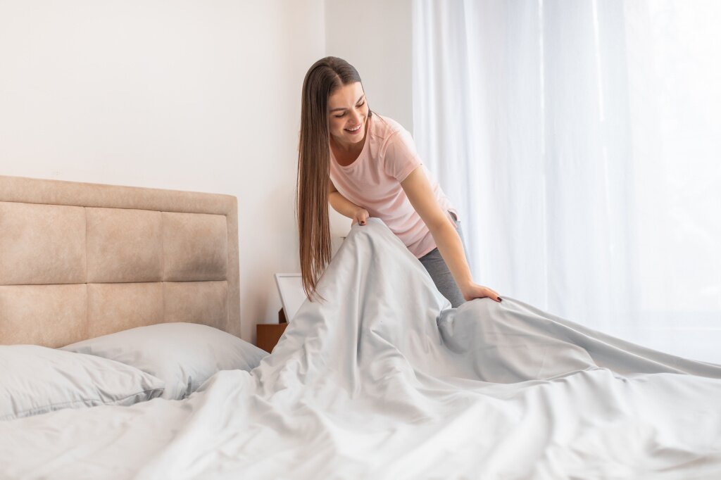 cheerful-woman-making-bed-bright-room-displaying-everyday-domestic-life.jpg