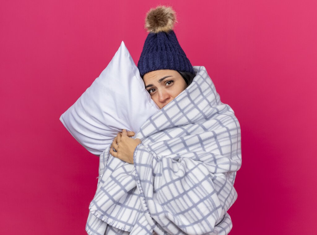 weak-young-caucasian-ill-girl-wearing-winter-hat-scarf-wrapped-plaid-hugging-pillow-putting-head-it-looking-camera-isolated-crimson-background-with-copy-space.jpg
