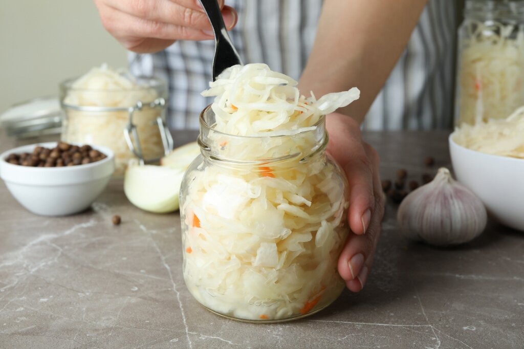 капуста в банке zensina-derzasaa-banku-s-kvasenoi-kapustoi-na-serom-teksturirovannom-stole-s-ingredientami.jpg