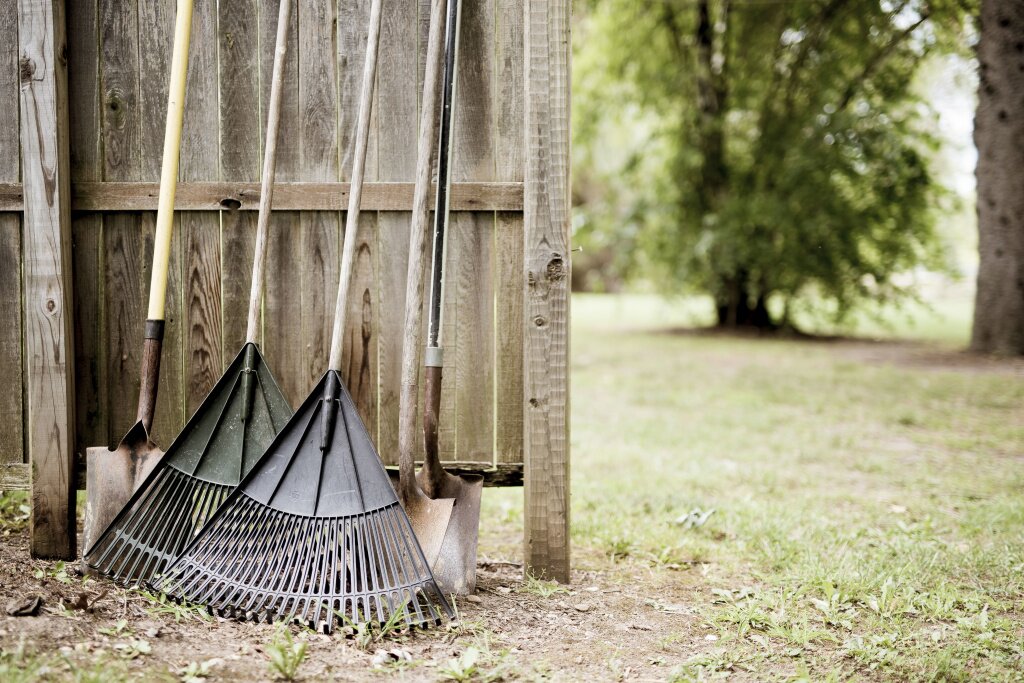 closeup-shot-two-leaf-rakes-shovels-leaned-against-wooden-fence-with-blurred-background.jpg