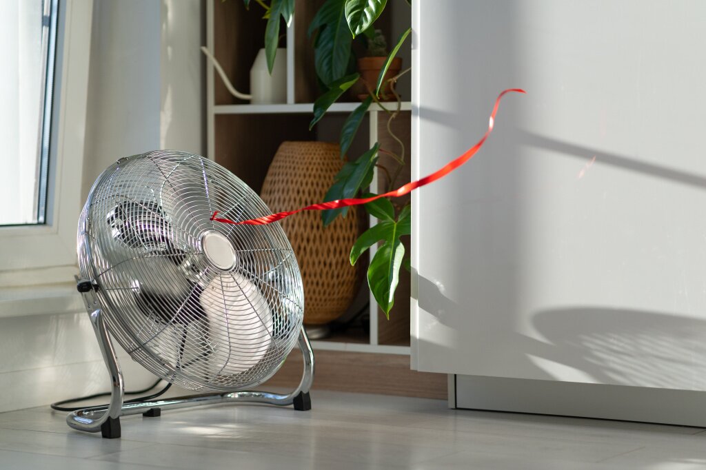 elektriceskii-ventilator-s-krasnoi-kacauseisa-lentoi-prednaznacennyi-dla-ohlazdenia-vozduha-i-podaci-vetra-raspolozennyi-vozle-okna.jpg