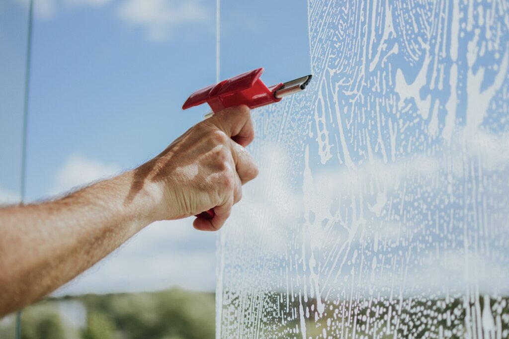 mans-hand-cleans-windows-balcony-with-detergents-tools-against-sky-trees.jpg